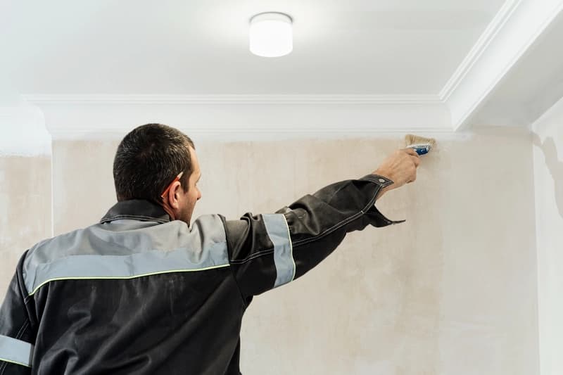 Artisan appliquant un apprêt sur les murs avant peinture, rénovation après sinistre
